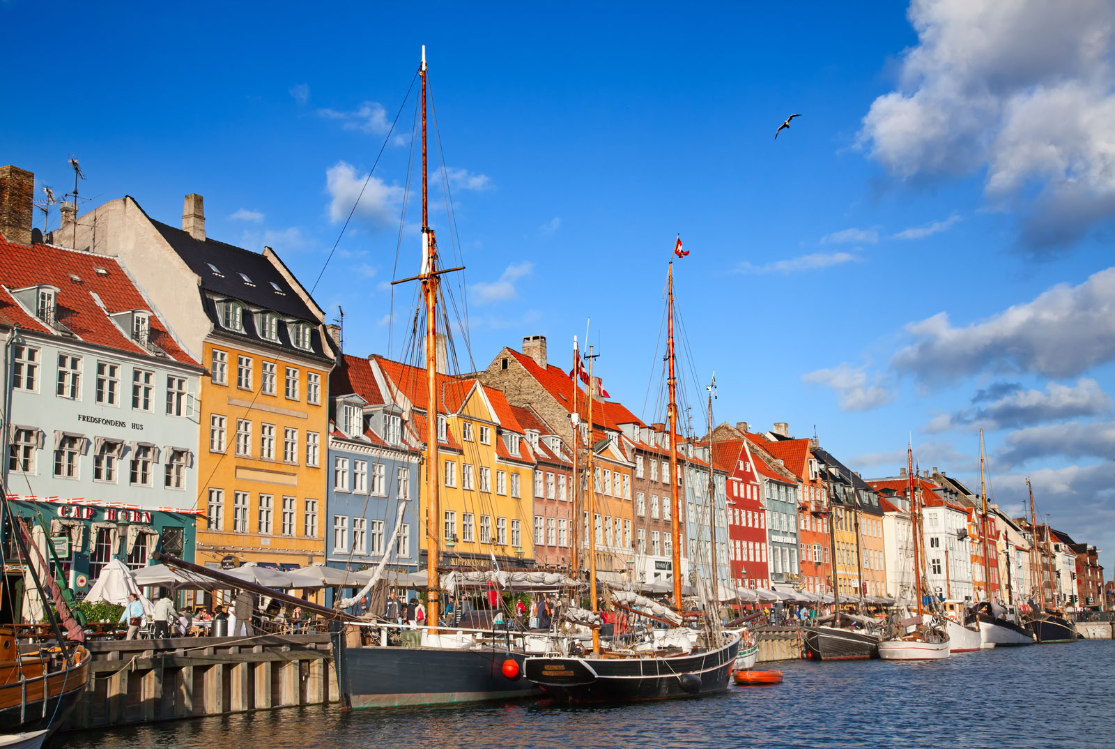 Colourful townhouses and moored wooden sailboats along Nyhavn canal in Copenhagen on a sunny day with blue sky.