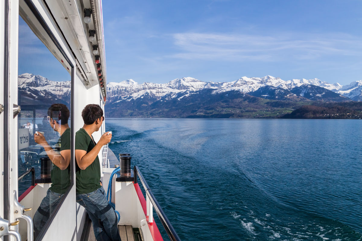 Passengers on a boat deck cruising Lake Thun with the snowy Bernese Alps behind