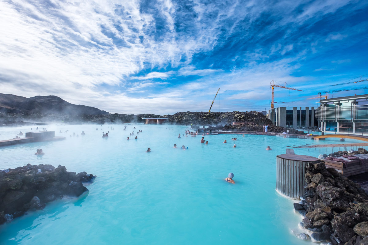 Bathers in a steaming milky-blue geothermal lagoon among lava rocks in Iceland