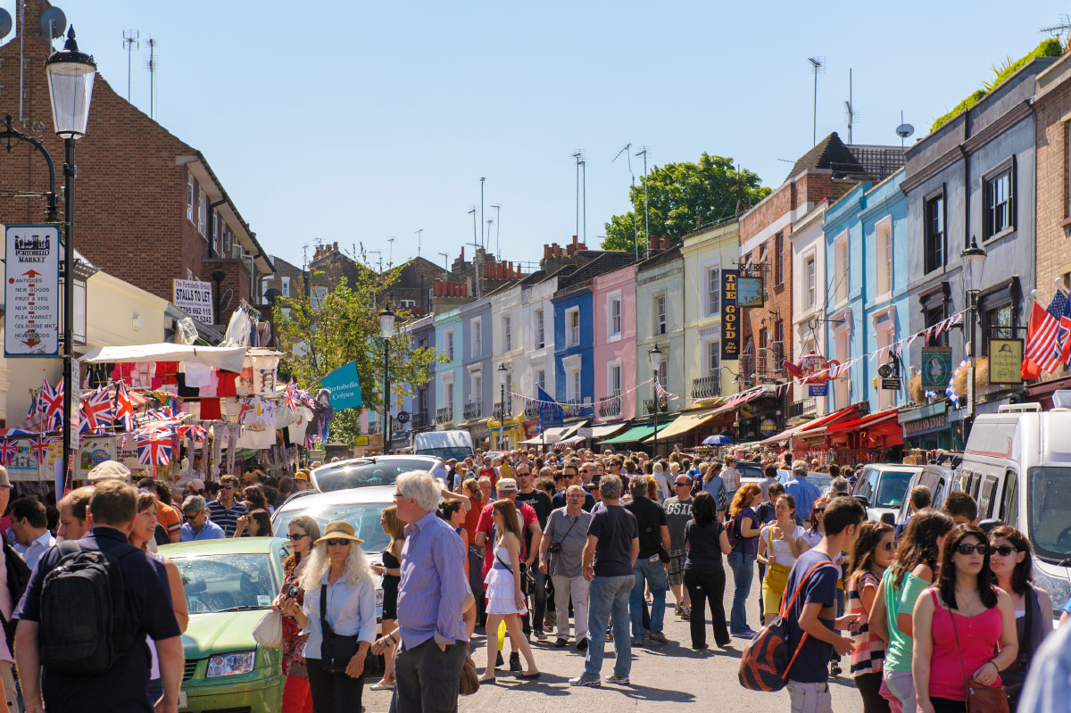 Crowds on Portobello Road market among pastel houses in Notting Hill, London
