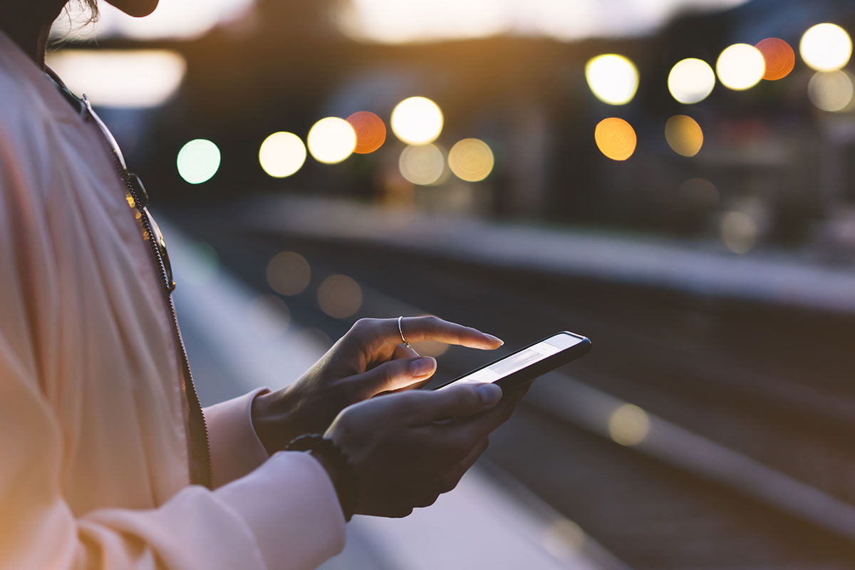 Woman using a smartphone on a train platform at dusk