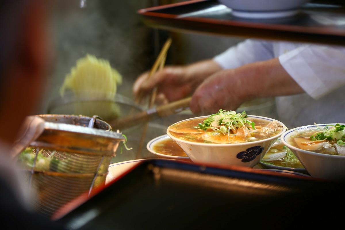 Chef serving bowls of ramen noodle soup across a counter in a Japanese ramen bar