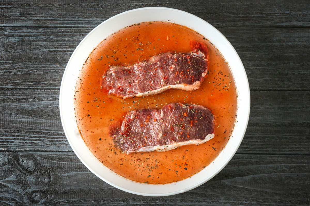 Two beef steaks soaking in a spiced miso marinade in a white bowl