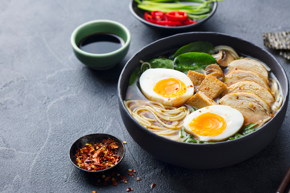 Bowl of chicken ramen with soft-boiled eggs, tofu and spinach beside chilli flakes