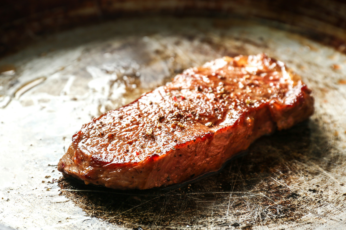 Seared steak with a caramelised crust sizzling in a hot pan