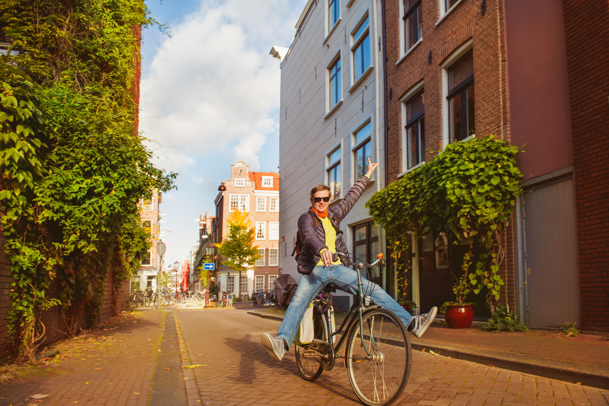 Man riding a bicycle with legs outstretched down a quiet Amsterdam street