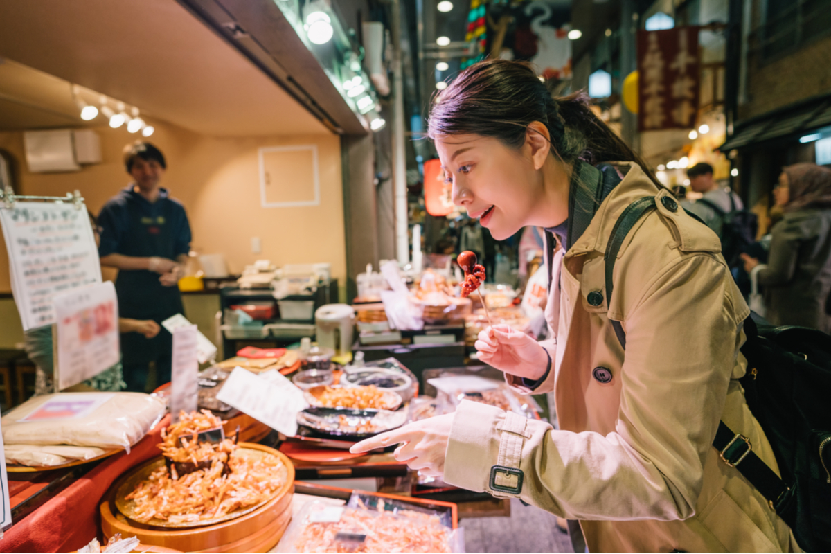 Woman tasting snacks at a stall in a busy covered food market in Japan