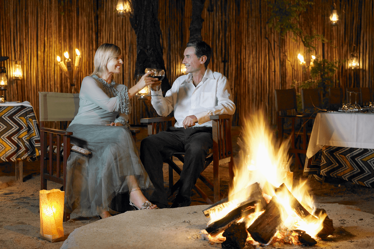 Happy couple enjoying wine next to fire on a South African safari