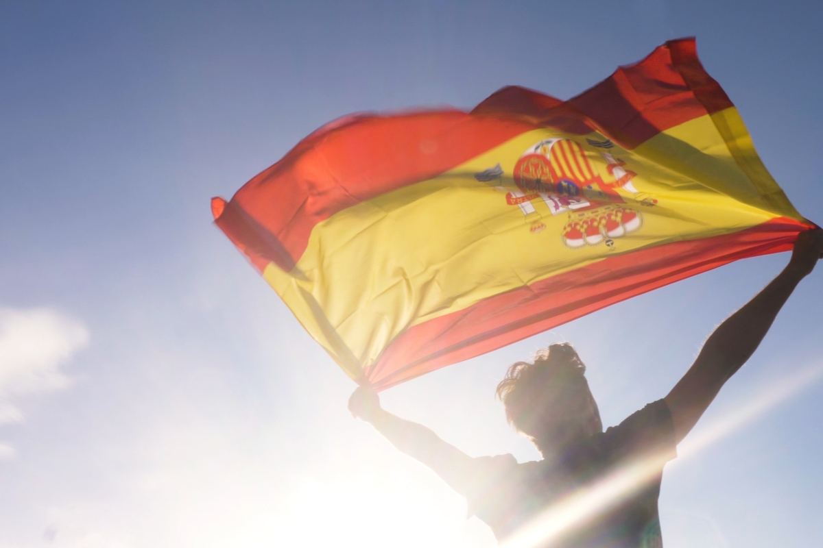 Man waves Spain flag against blue sky