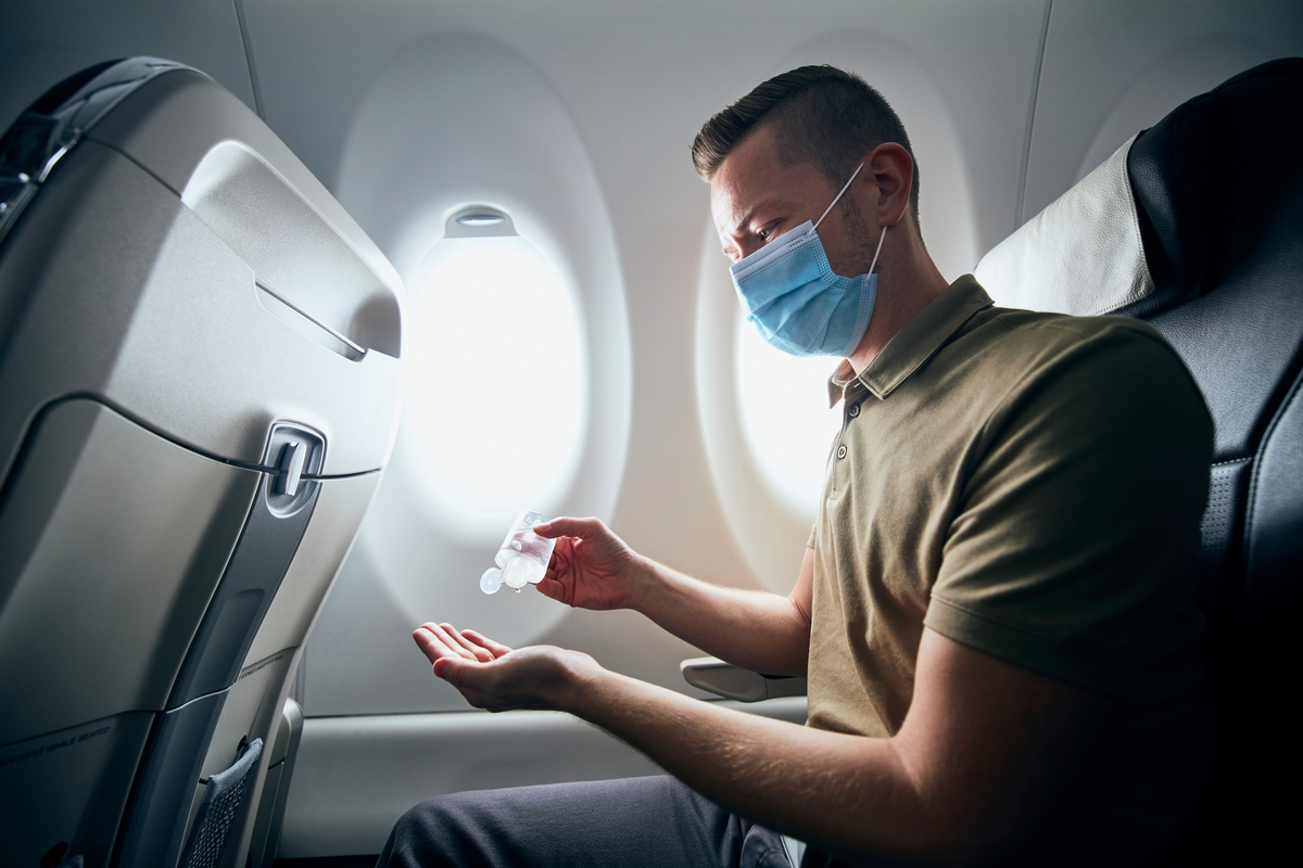 Man wearing a face mask cleaning his hands with sanitiser in a plane seat