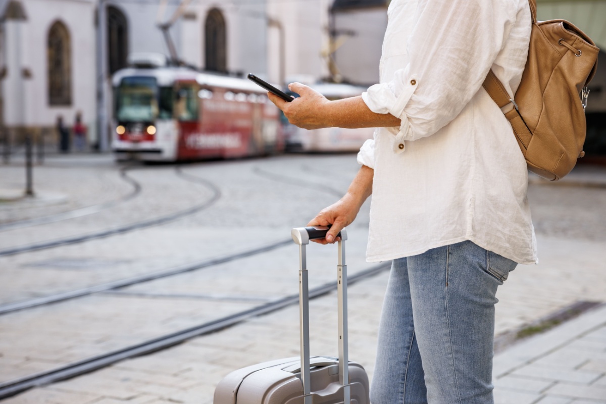 Woman with a suitcase and phone beside tram tracks in a European old town